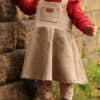 Kind steht draußen mit einem roten Shirt und einem Latzkleid, genäht nach dem Schnittmuster "Twirly Latz" von Schleiferlwerk