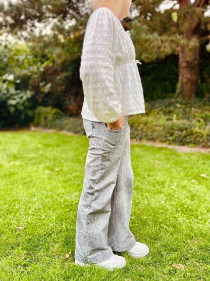 Schnittmuster Wide Legs: hellgraue Baggy Hose mit Eingrifftasche und weiße Bluse, seitlich auf dem Rasen.