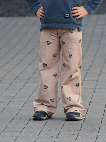 Beige selbst genähte weite Hose mit schwarzen Herzen und dunkelblauem Pullover auf Pflaster.