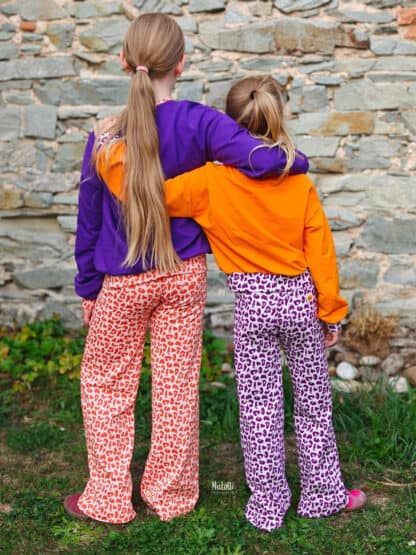 Zwei Mädchen Arm in Arm von hinten in selbst genähten Baggy Hosen mit Leomuster.