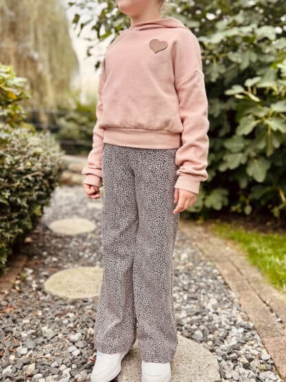 Weite Hose mit kleinem schwarzem Leomuster und rosa Pullover am Gartenweg.