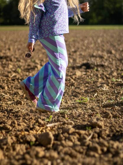 Selbst genähte Wide-Leg-Hose mit lila-grünen Schrägstreifen beim Laufen über einen Acker.