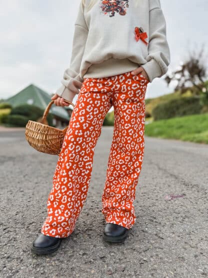 Orange gemusterte weite Hose mit cremefarbenem Pullover und Weidenkorb in der Hand.