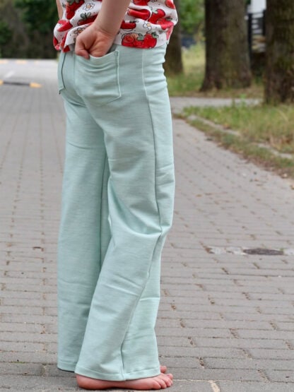 Mintgrüne Wide-Leg-Hose von hinten, barfuß auf Pflaster, eine Hand in der Po-Tasche.
