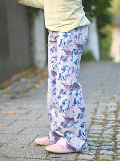 Weiße selbst genähte weite Hose mit blau-lila Einhorn-Muster auf Kopfsteinpflaster.