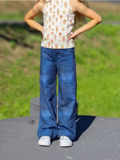 Jeansblaue Wide-Leg-Hose mit Eiscreme-Shirt, die Hände in die Hüften gestemmt.