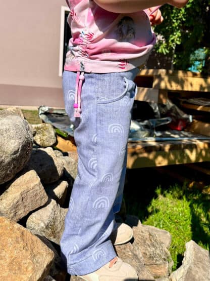 Selbst genähte Baggy Hose in hellem Lila mit Regenbogenmotiven zwischen Steinen.