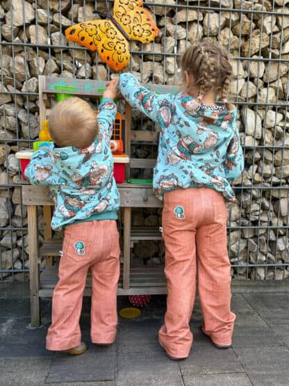 Schnittmuster Wide Legs: zwei Kinder in lachsfarbenen Baggy Hosen an einer Matschküche.