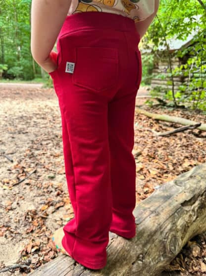 Rote Baggy Hose mit Po-Taschen und Label auf einem Baumstamm, genäht nach dem Schnittmuster Wide Legs.