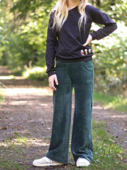 Dunkelgrüne Baggy Hose aus Cord mit schwarzem Pullover auf einem Waldweg.