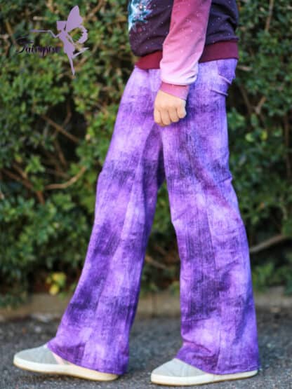 Lila selbst genähte weite Hose in Jeansoptik mit pinkem Oberteil vor einer Hecke.