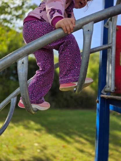 Beim Klettern am Geländer: lila gepunktete weite Hose mit rosa Pullover.