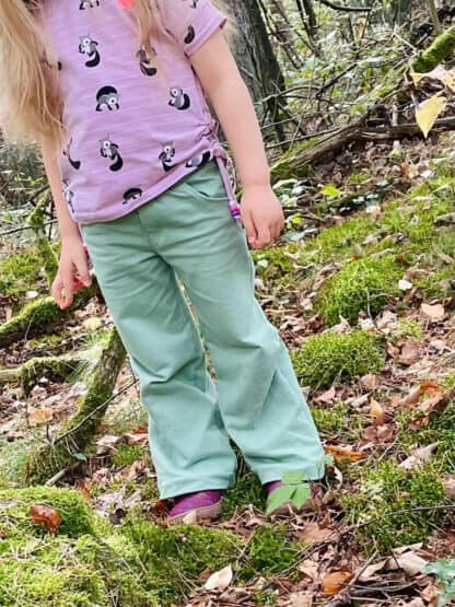 Schnittmuster Wide Legs: mintgrüne Baggy Hose mit lila Shirt im Wald auf Moos.