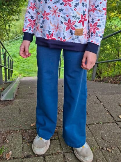 Blaue weite Jogginghose mit Weihnachtsstern-Pullover auf einem gepflasterten Platz.