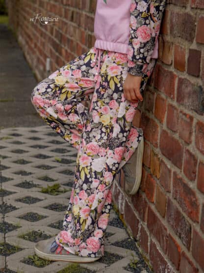 Schnittmuster Wide Legs: dunkle weite Hose mit rosa Blüten an einer Backsteinmauer.